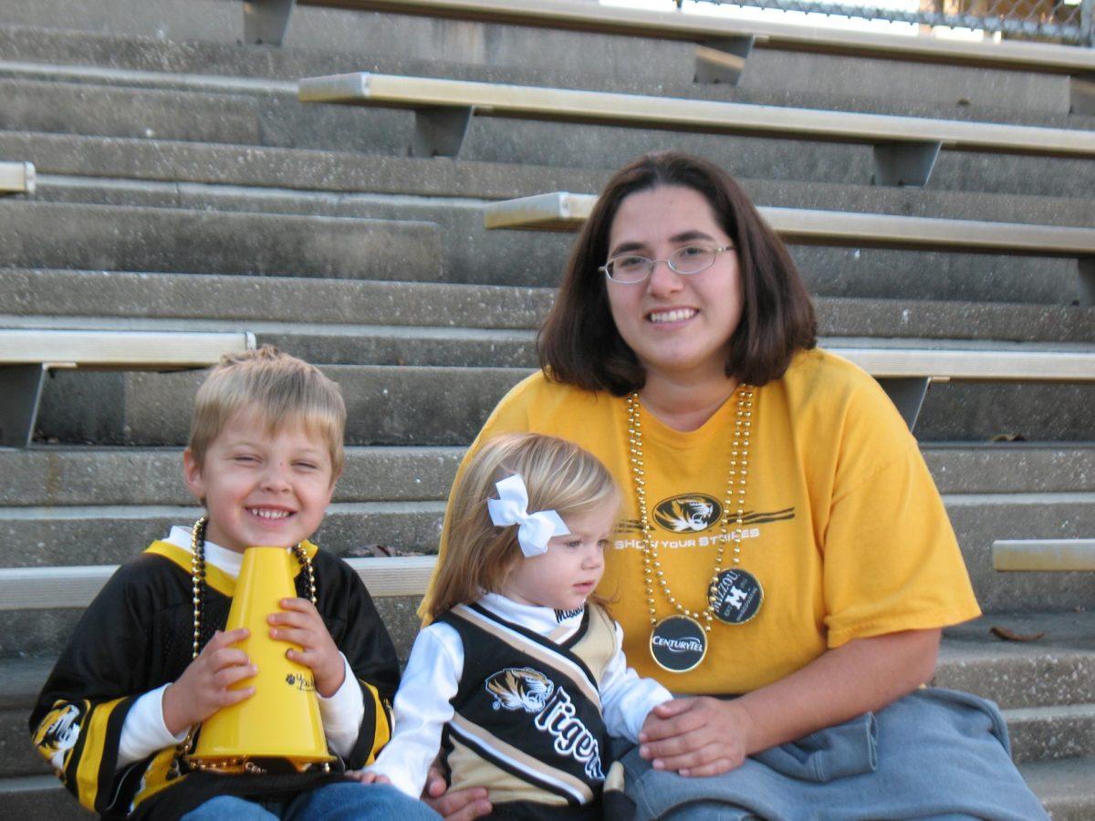 A woman poses with two children, all weawring Mizzou themed shirts and necklaces.