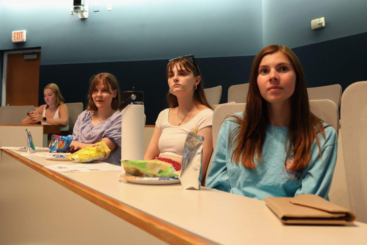 Three students observe a presentation by Women in Media executive board members.