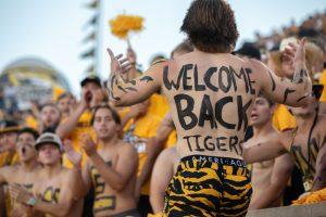 A student with body paint on his torso, gestures towards the crowd by raising his arms up.