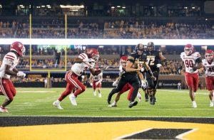Missouri football player is surrounded by South Dakota football players as he approaches the endzone.