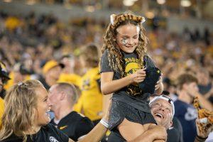 An attendee of the Missouri football game sits on her father's shoulders, smiling at the t-shirt in her hands.