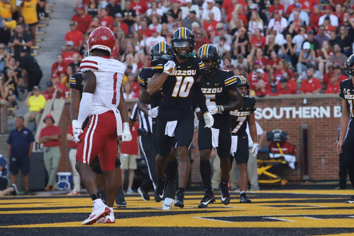 A Missouri football player runs and smiles as other Missouri players run behind him.