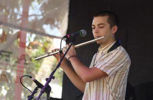 A man stands in front of a microphone and plays his flute.