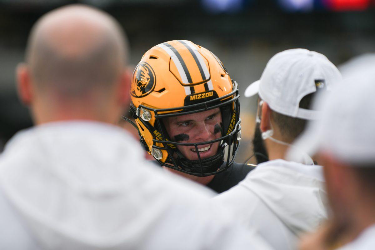 A Missouri football player talks to two men wearing white.