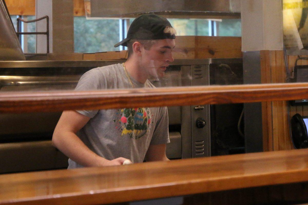 Man rolls dough behind a glass panel.
