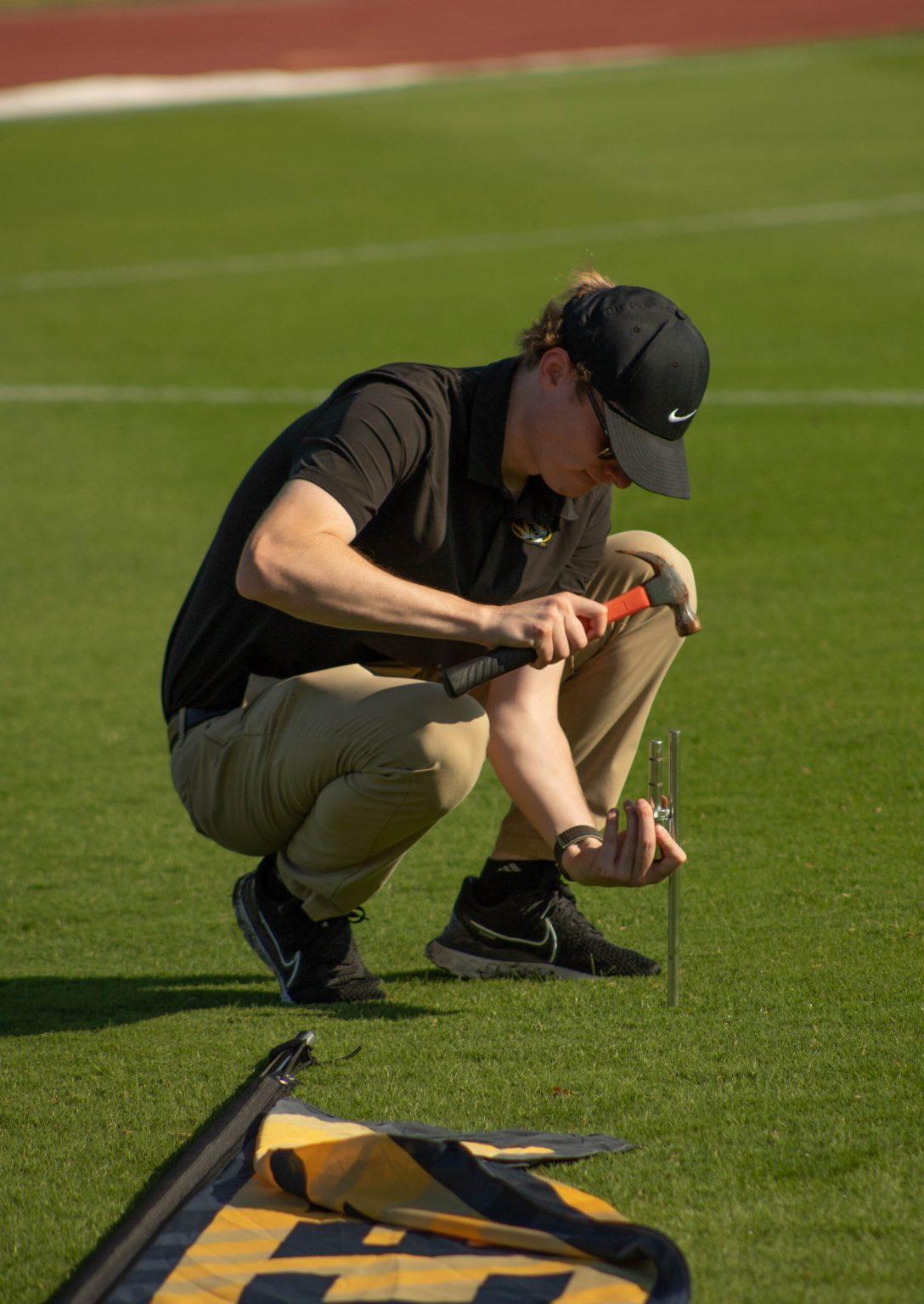 A man hammering a pipe into a turf field.