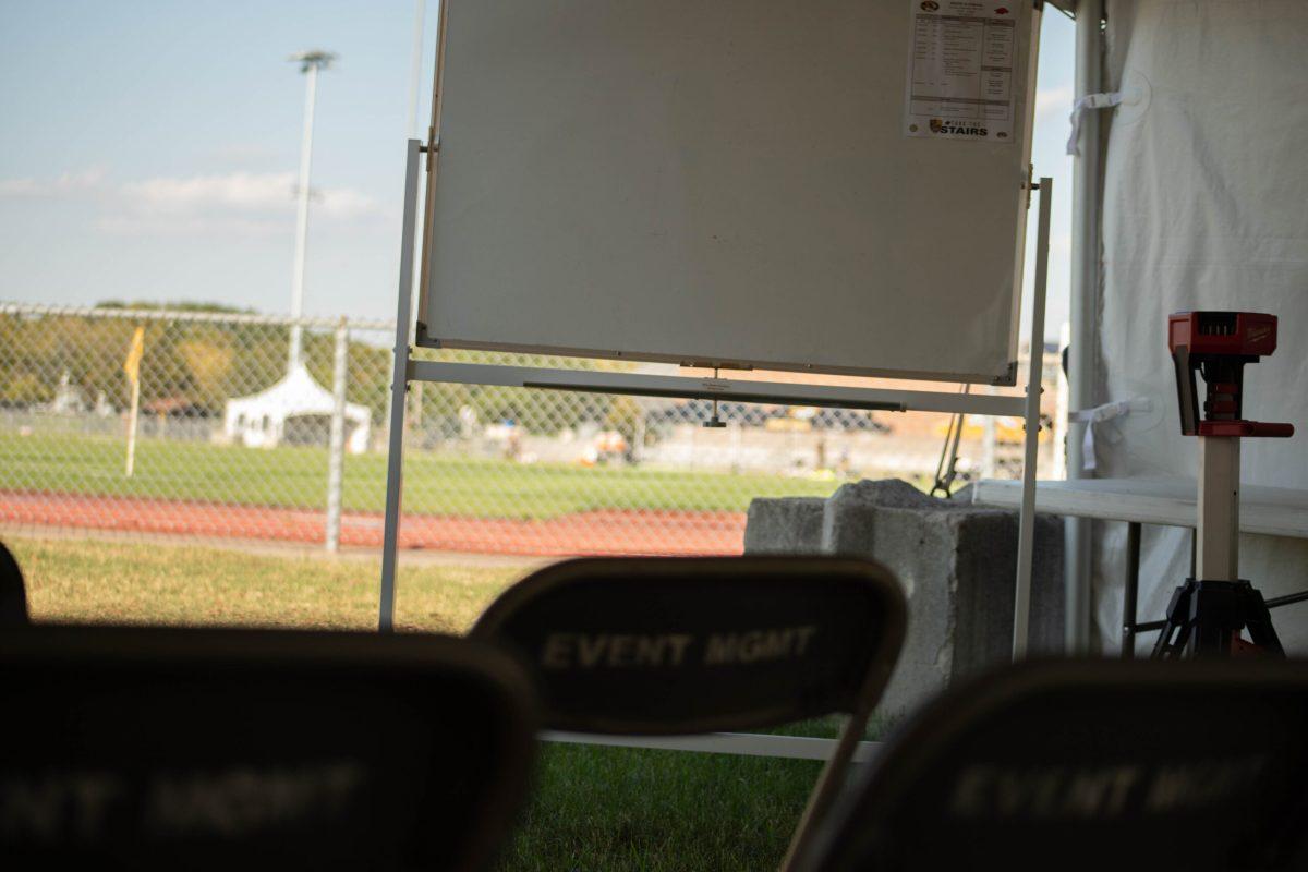 A whiteboard in front of a set of chairs inside a tent at the soccer stadium.