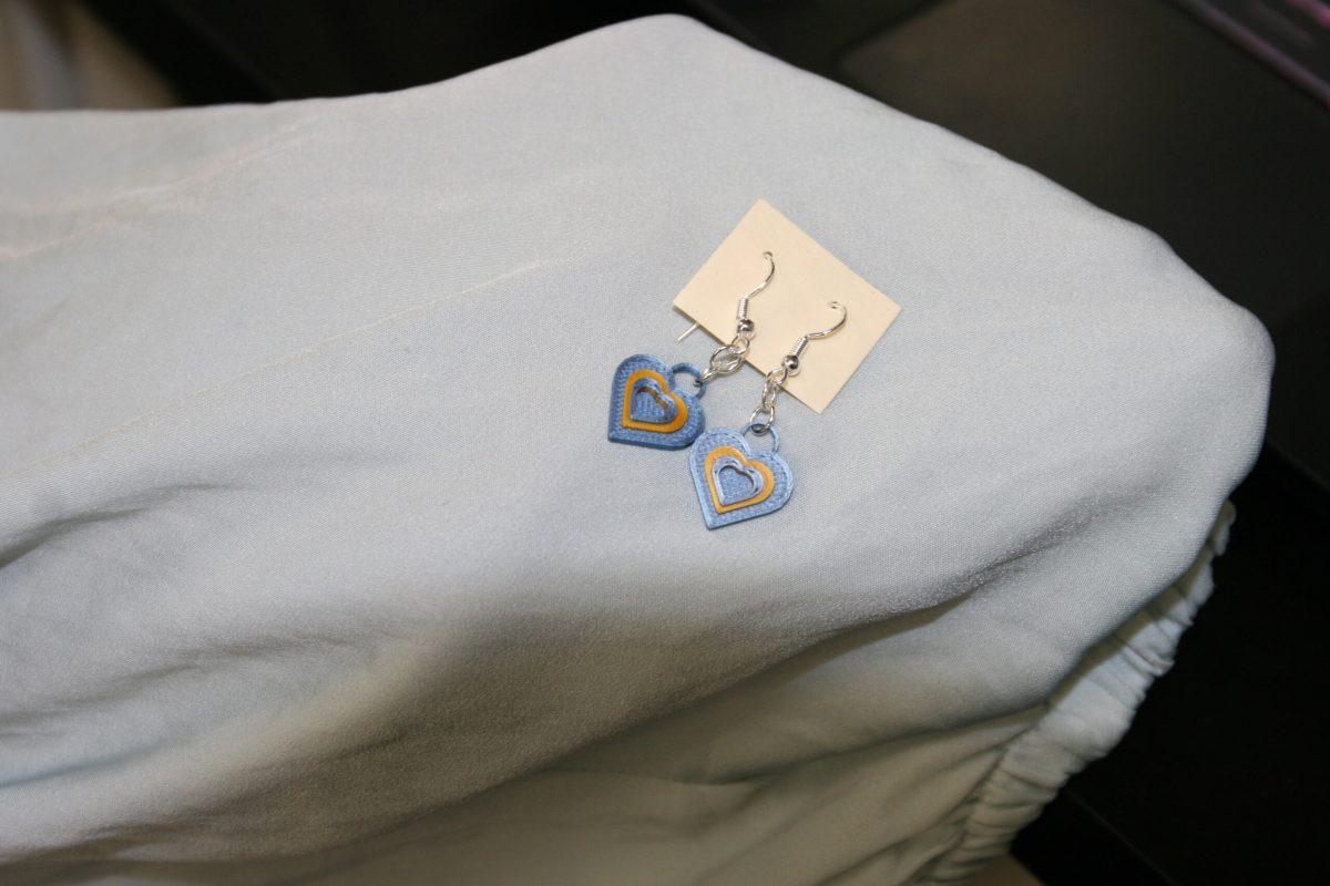 A pair of heart earrings in Ukrainian colors, blue and yellow, are displayed on a shirt sleeve in the 3D printing lab at Lafferre Hall.