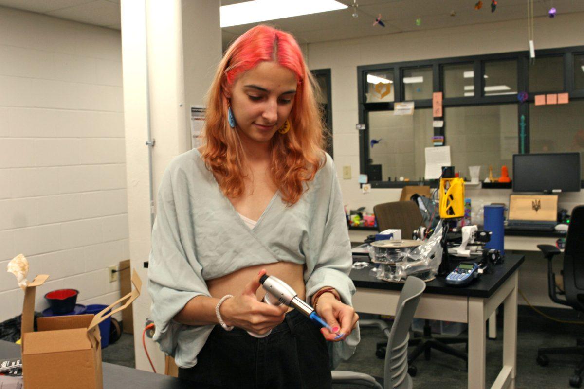 Alina Rohulia stands and puts a flame from a heater  to a 3D printing design she just finished in the 3D printing lab of Lafferre Hall.
