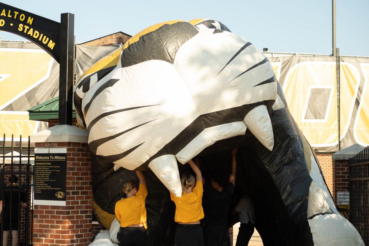 Large inflatable tiger head being held up by a pair of women in yellow shirts.