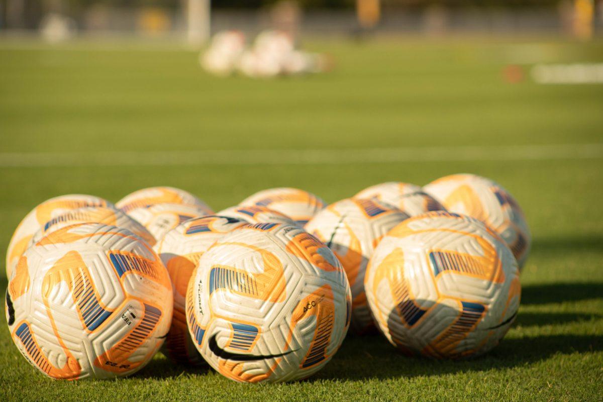 Soccer balls sitting in a group on a soccer field.