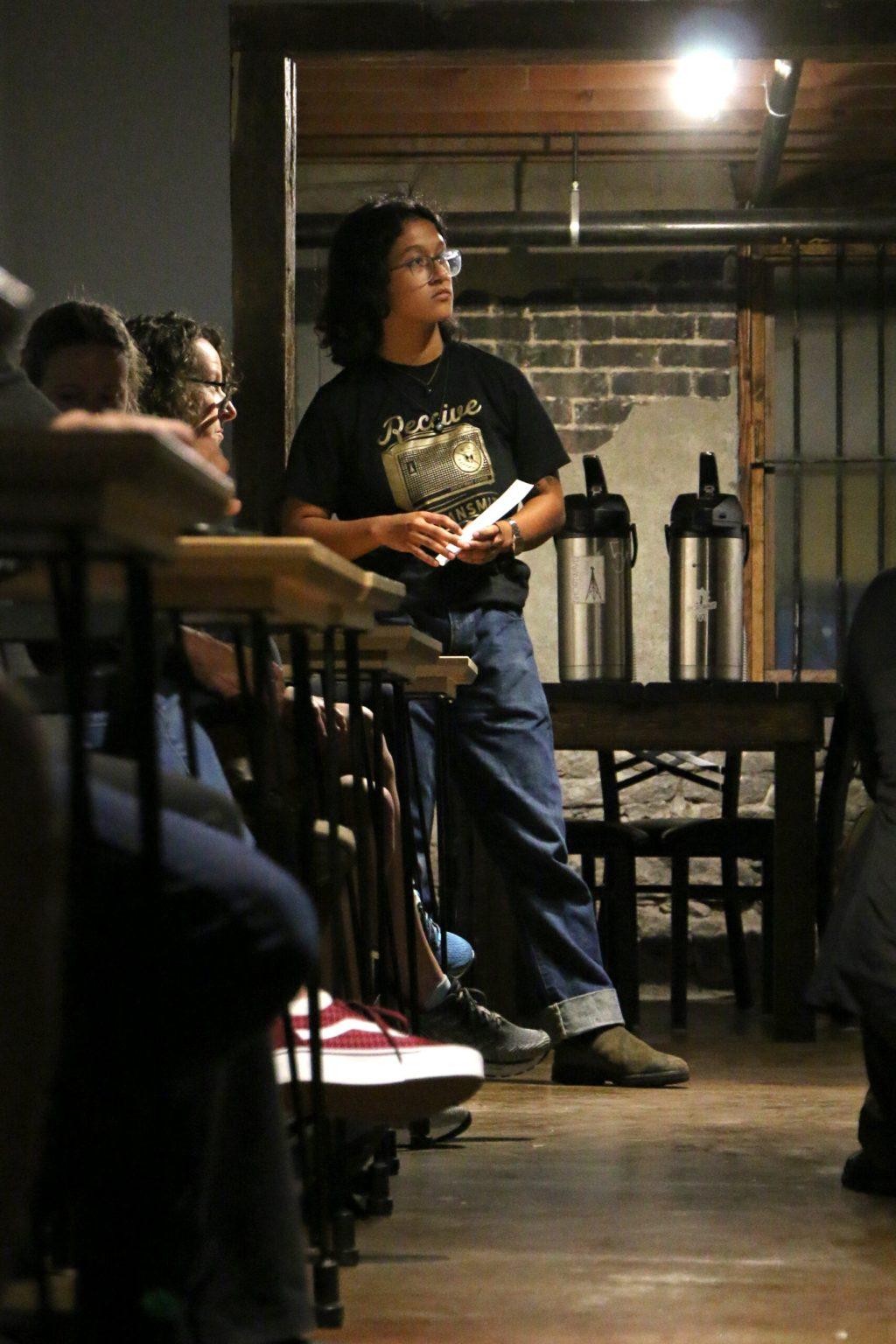 Ana Manzano leans on a door frame while holding a sheet of paper rolled up in her hand.
