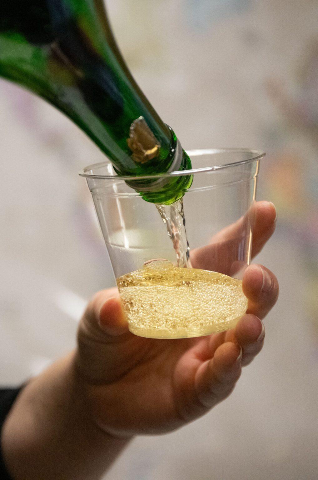 A volunteer pours sparkling yellow grape juice into a small clear plastic cup. 