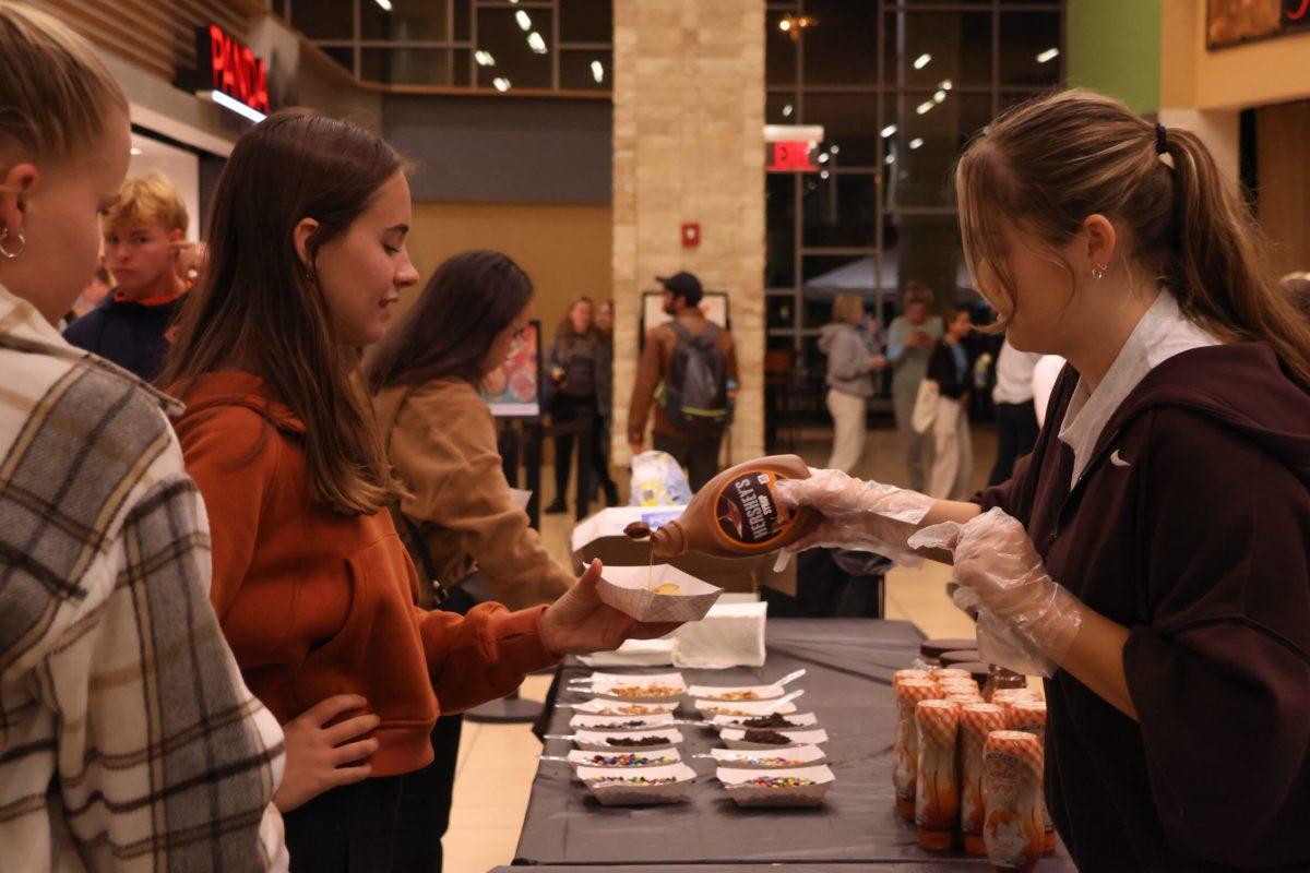 A volunteer squeezing caramel onto a student’s dish of apple slices.