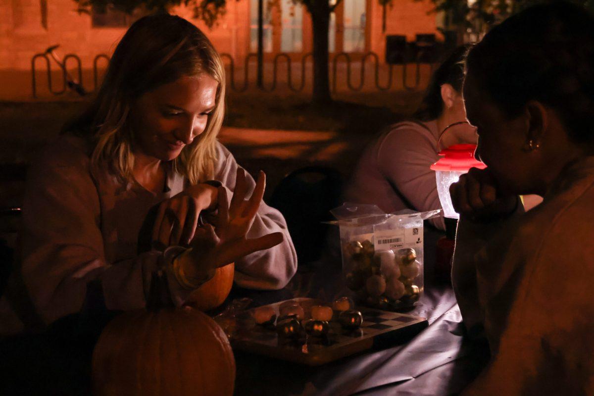 Two students play a game of checkers with pumpkin game pieces.