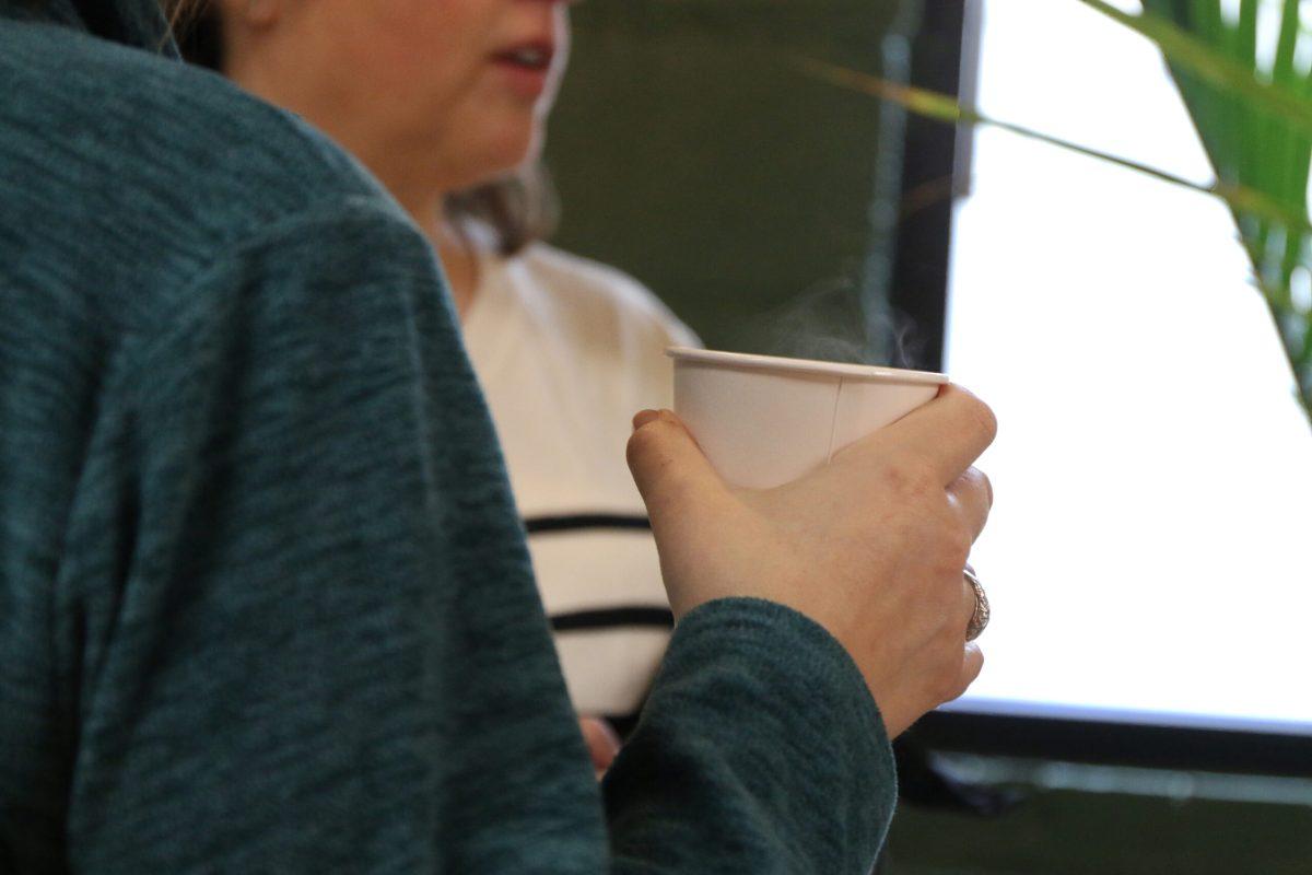 A crawler holds a white steaming cup of coffee in their right hand. 
