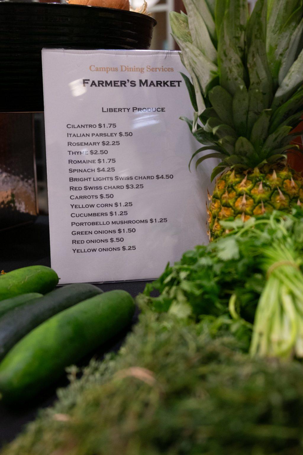 A list of prices sits on a table behind various produce.