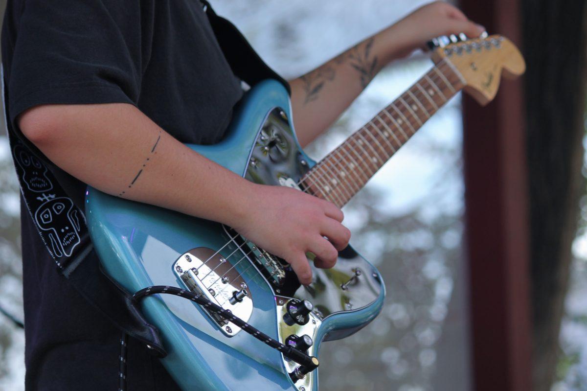 A blue guitar with hands playing on the strings.