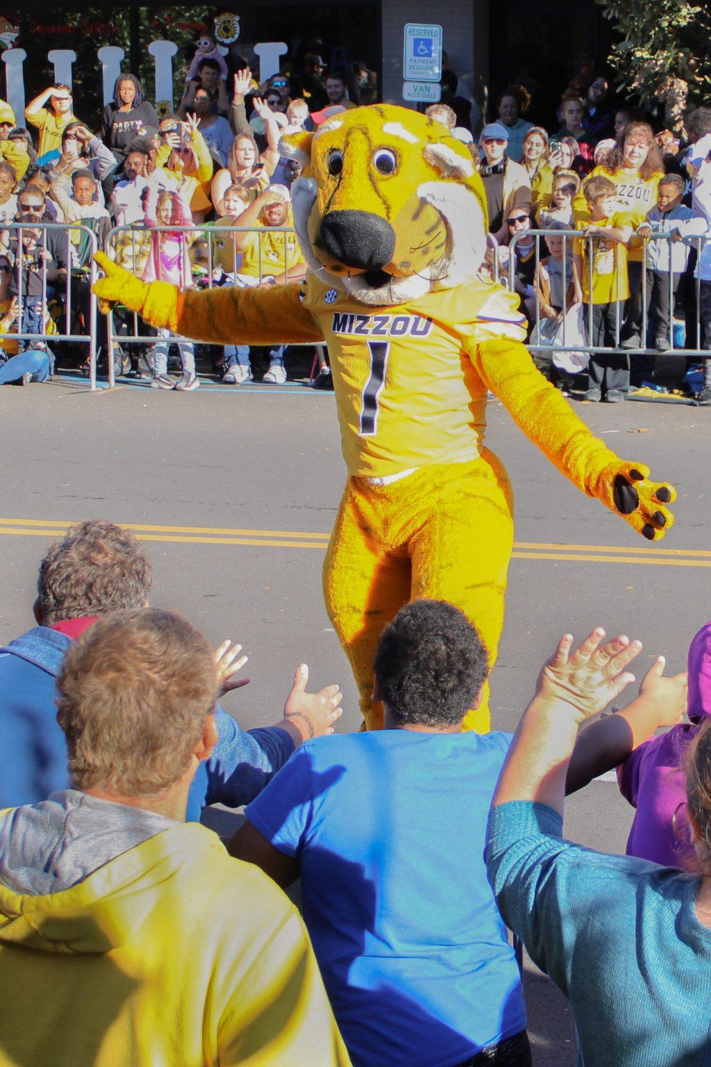 Truman the Tiger mascot opens his arms to greet fans on the side of a road.