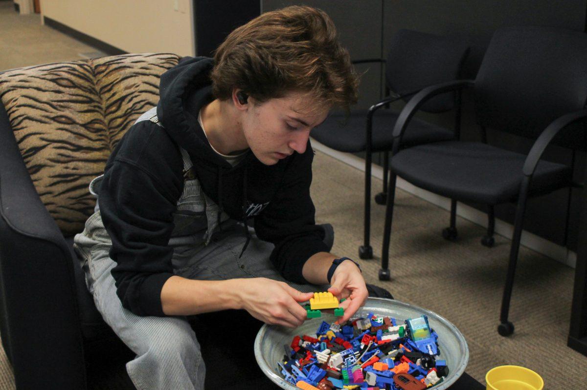 Person puts legos together in front of a bowl filled with legos.
