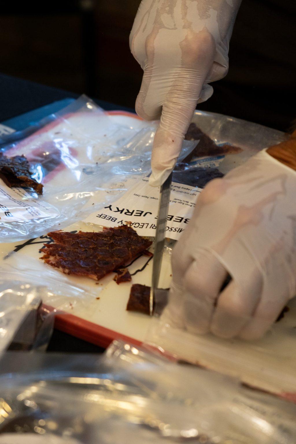 A man cuts up pieces of beef jerky on a cutting board.
