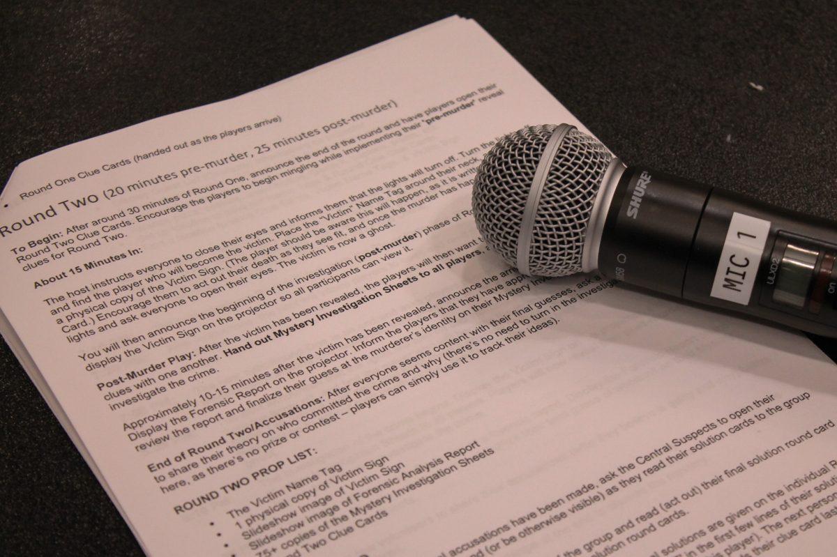 A piece of paper full of writing lays on a table under a microphone.
