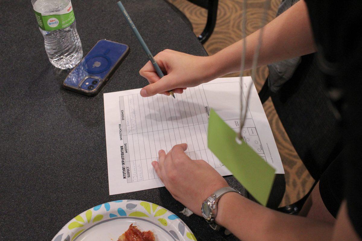 Someone holds a pencil as they are writing notes on a piece of paper.