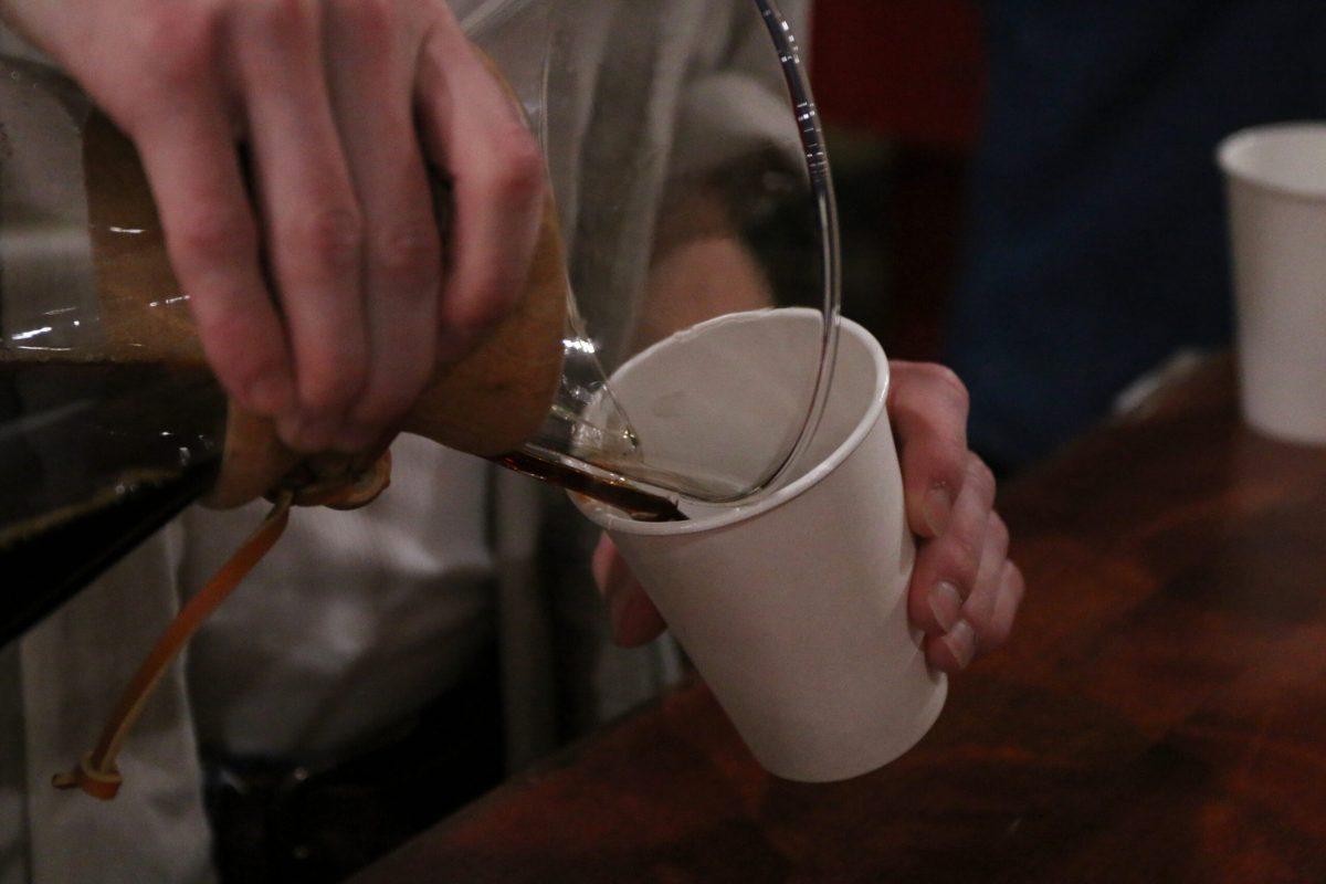 Colin McElduff’s hand pours a Chemex of black coffee into a white paper cup.
