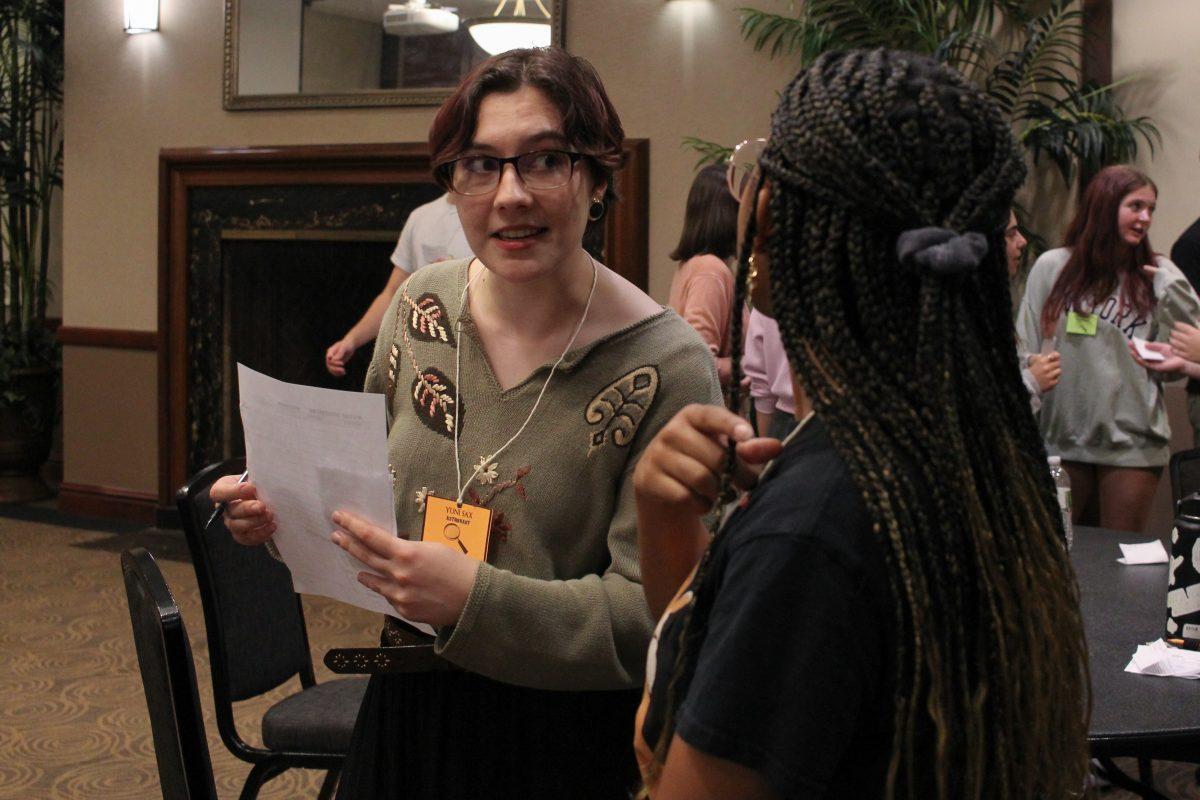The photo shows a girl curiously looking at another student as she holds her noted paper close to her body.