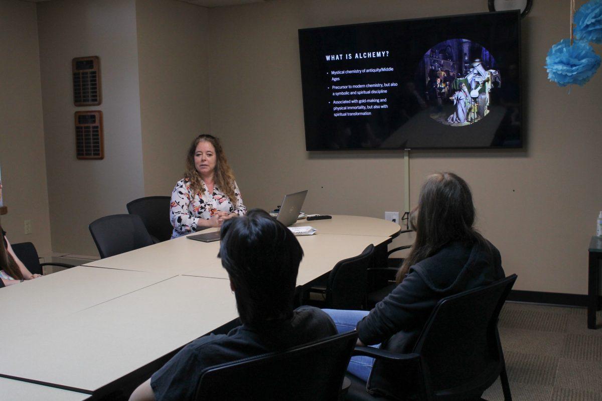 Woman talks in front of a screen as students watch her and the slideshow presentation.