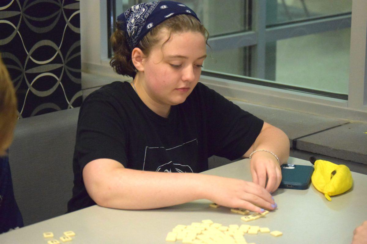 A student is sitting in a booth moving around letter pieces scattered in front of them on a table.