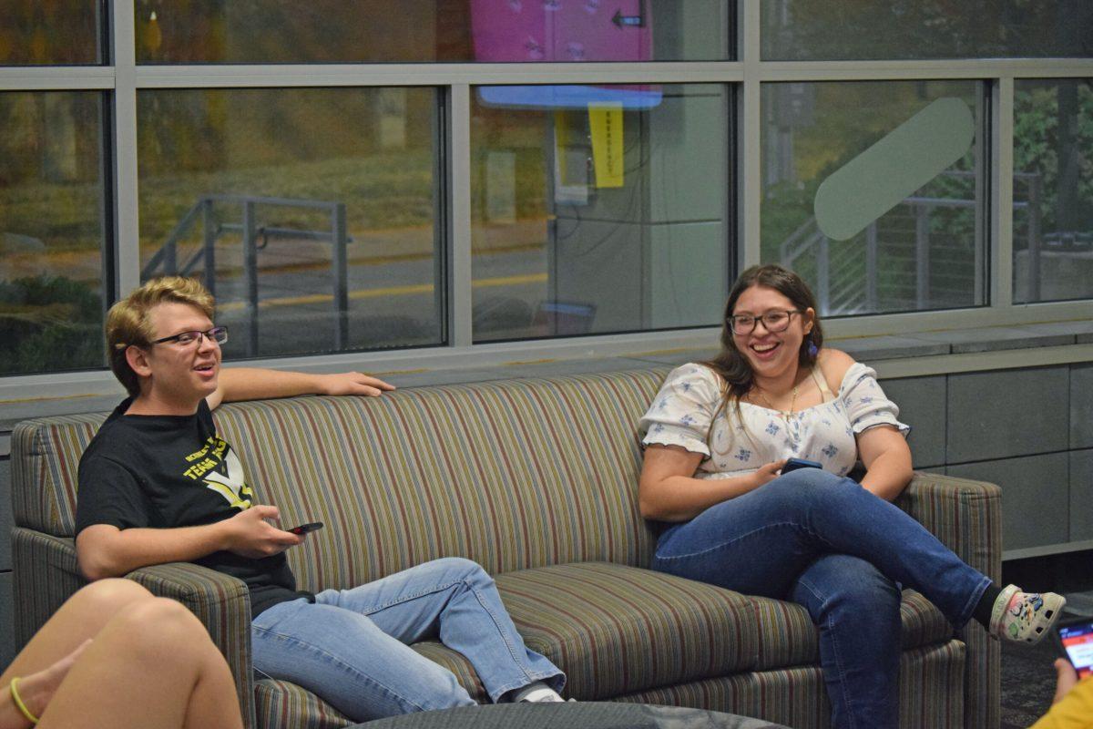 Two students are sitting and laughing in a residence hall lobby.