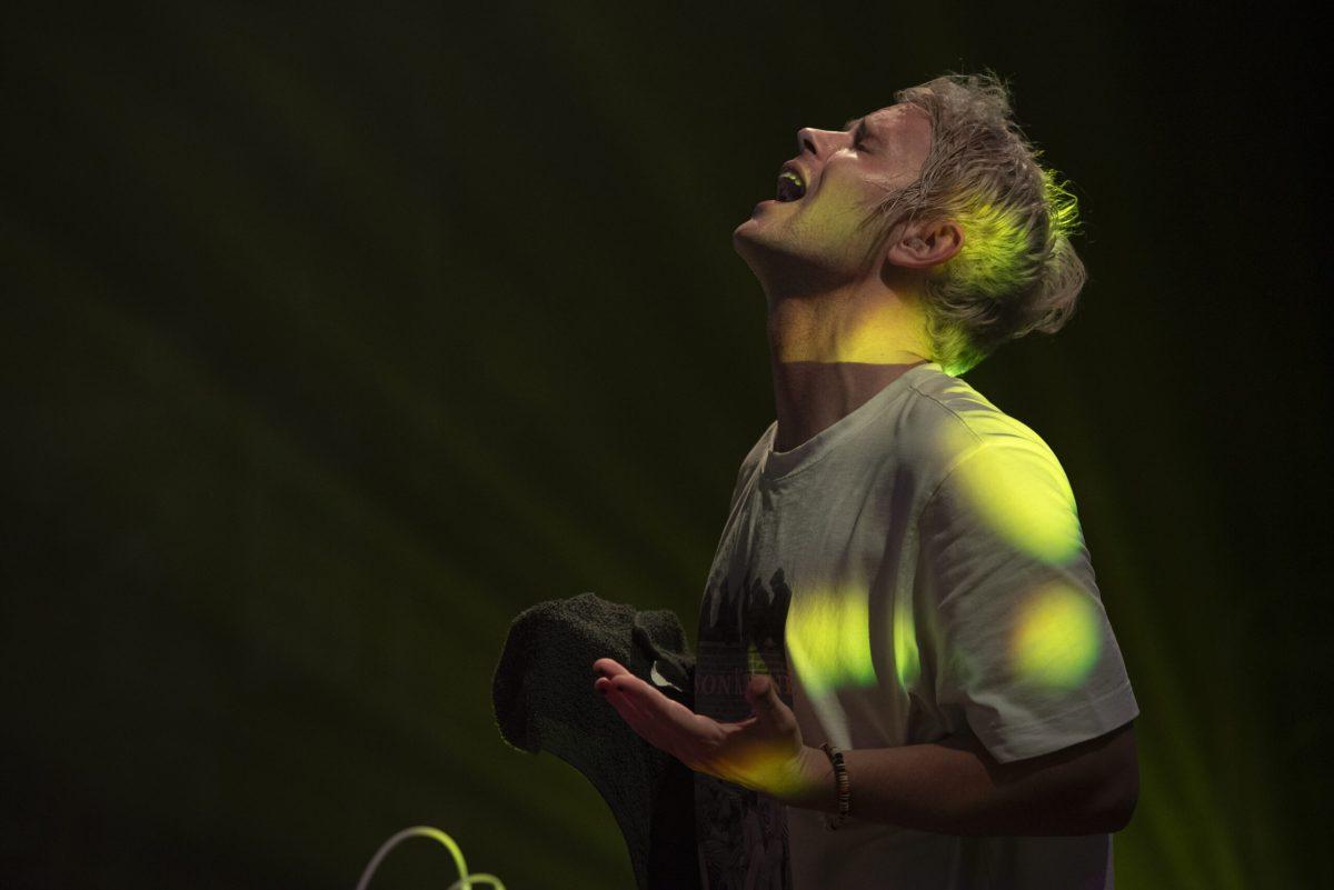 A man holds a black towel and sings with his eyes closed.