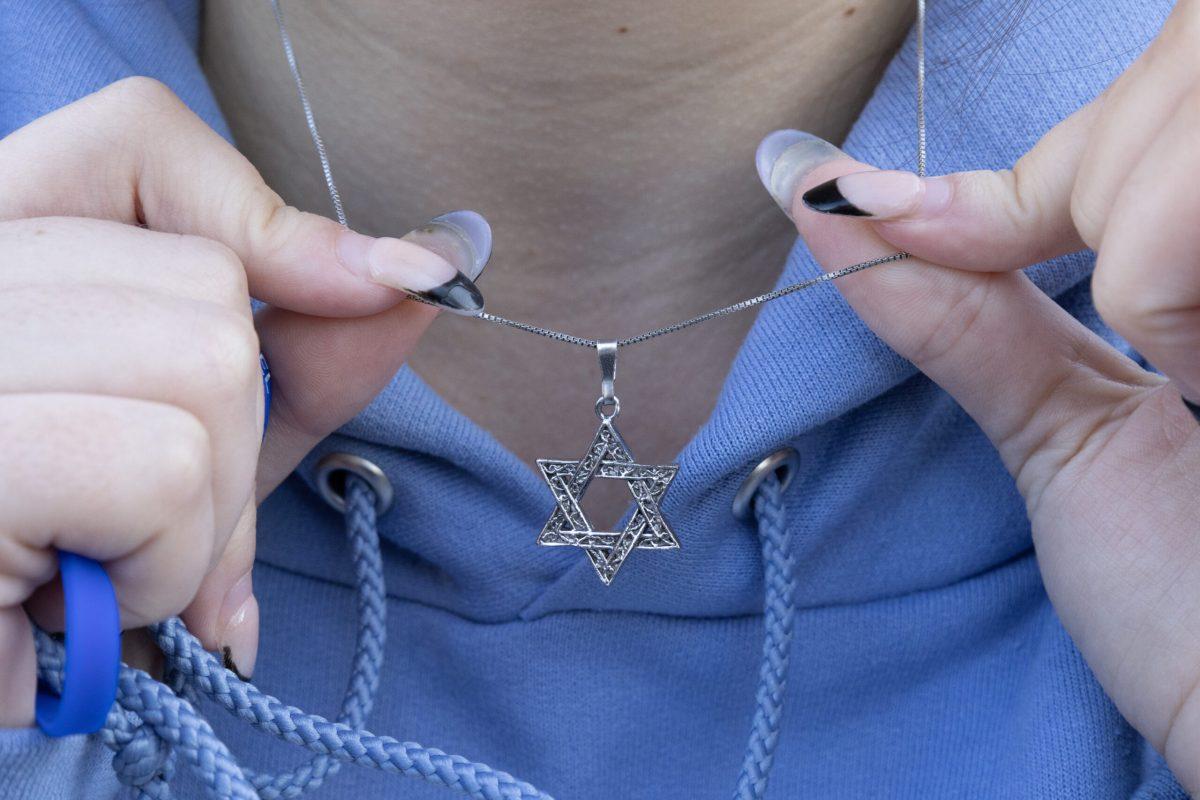 A close-up of hands holding up a necklace with a Star of David symbol.
