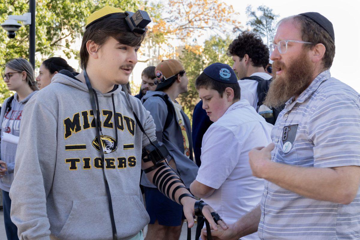 A man with tefillin wrapped around his arm and head recites blessings with another man.
