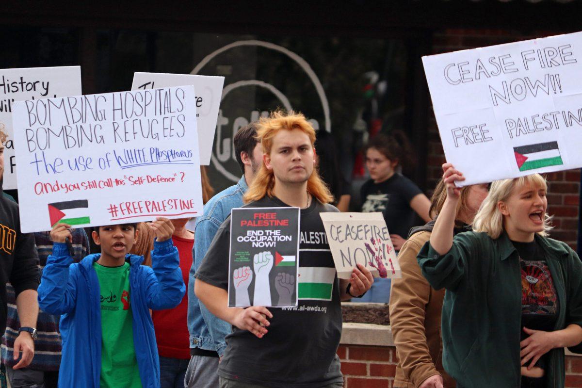 A man walks with a group of protestors, holding two signs that say “Free Palestine, end the Occupation Now,” and “Ceasefire Now.”