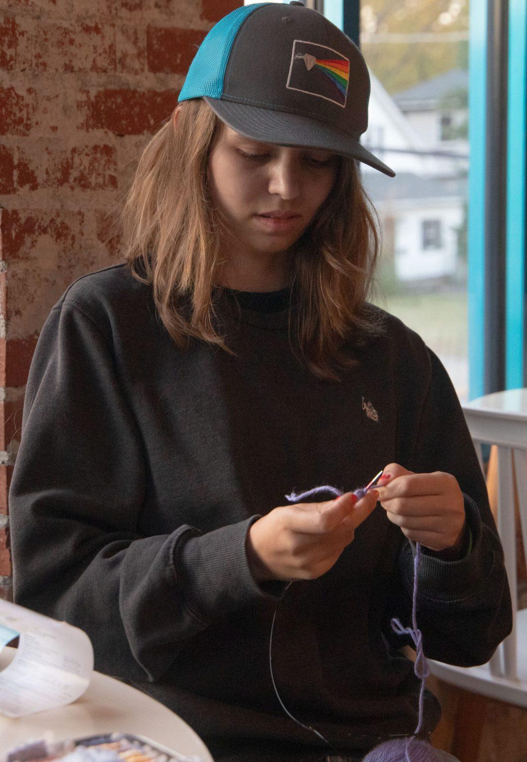 Lila Rowzee knits with a knitting needle and purple yarn.
