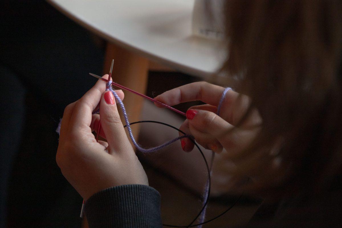 Lila Rowzee holds two needles to knit purple yarn.
