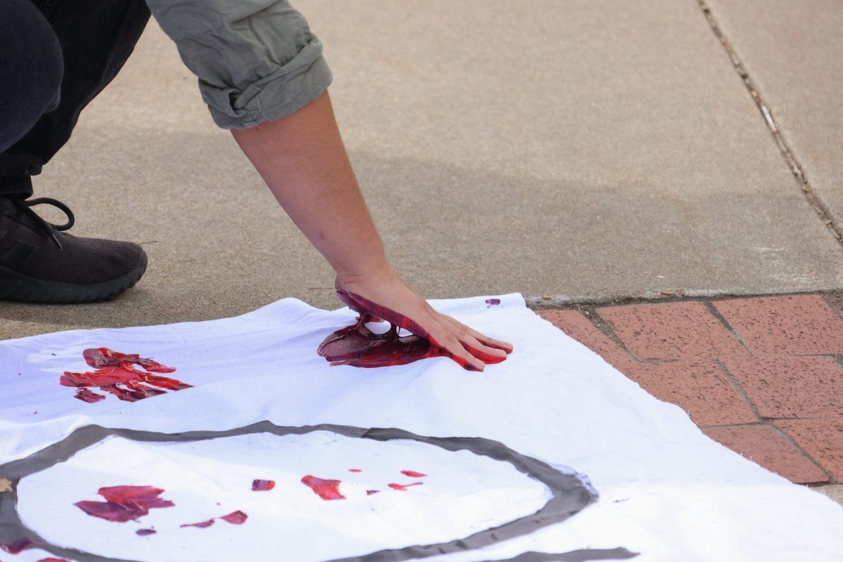 A protestor making a red handprint on a cloth that reads “our tax dollars.”
