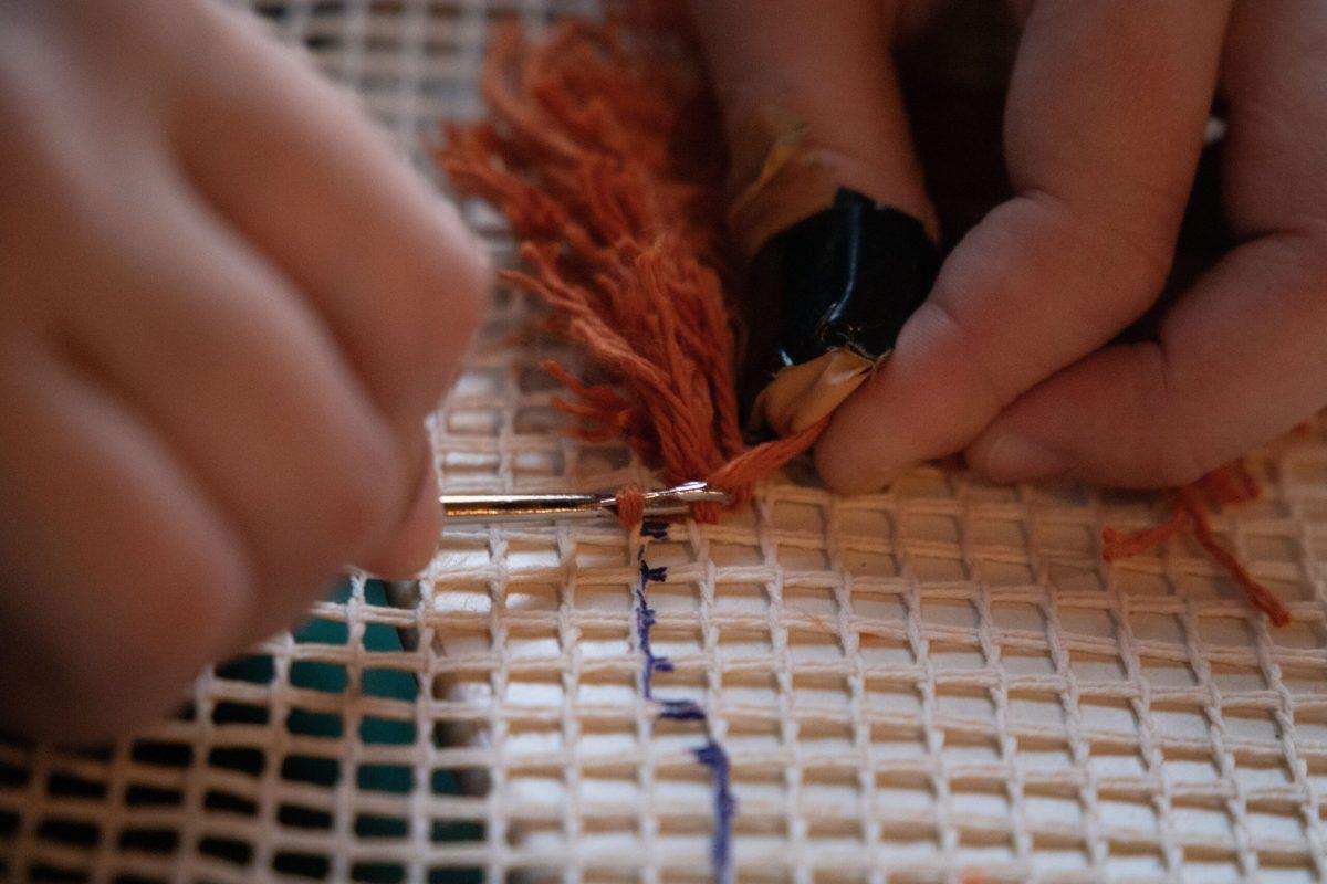 Robyn Hayes uses a hook to embroider yarn into her weaved canvas.

