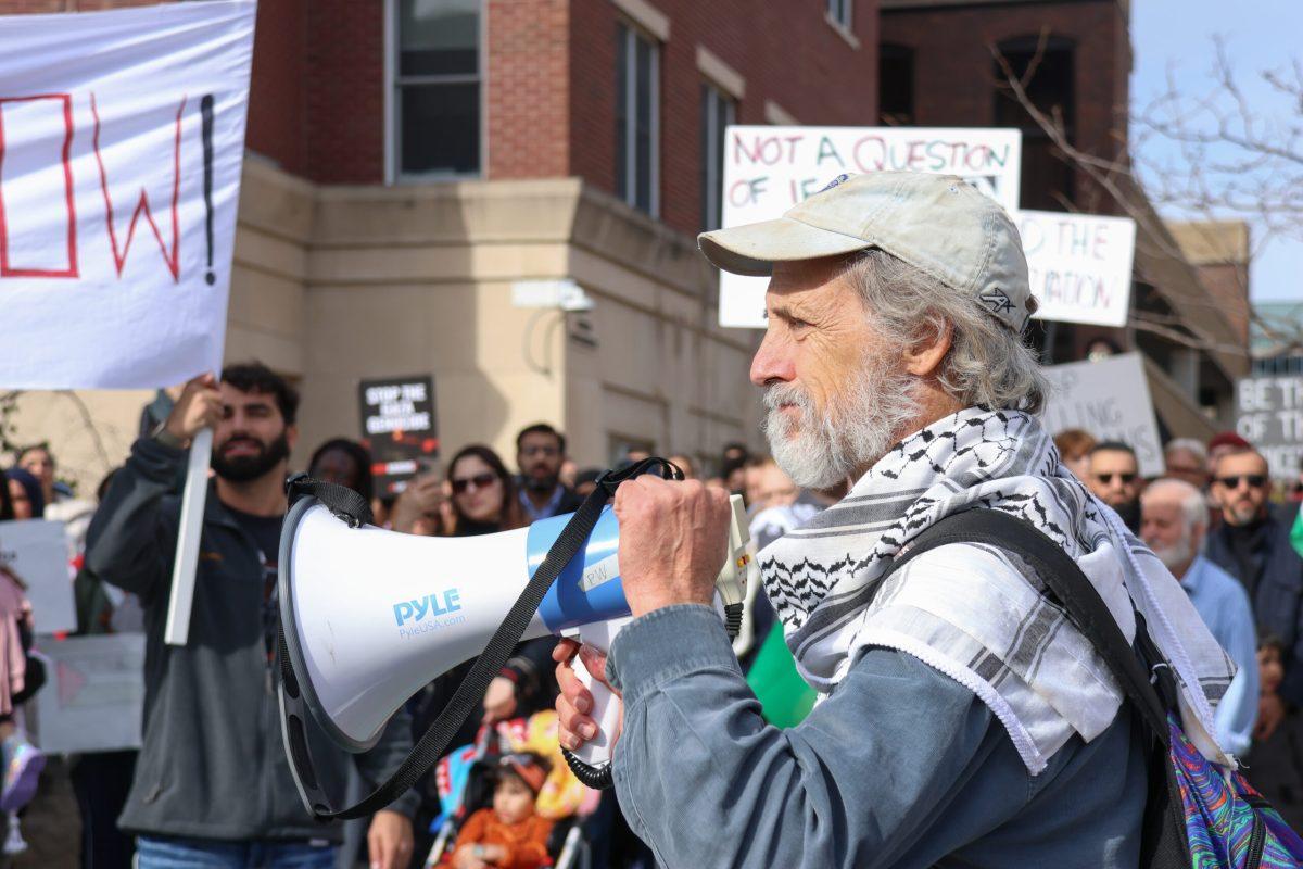 A man holding a megaphone raising his fist in front of a crowd of protestors.
