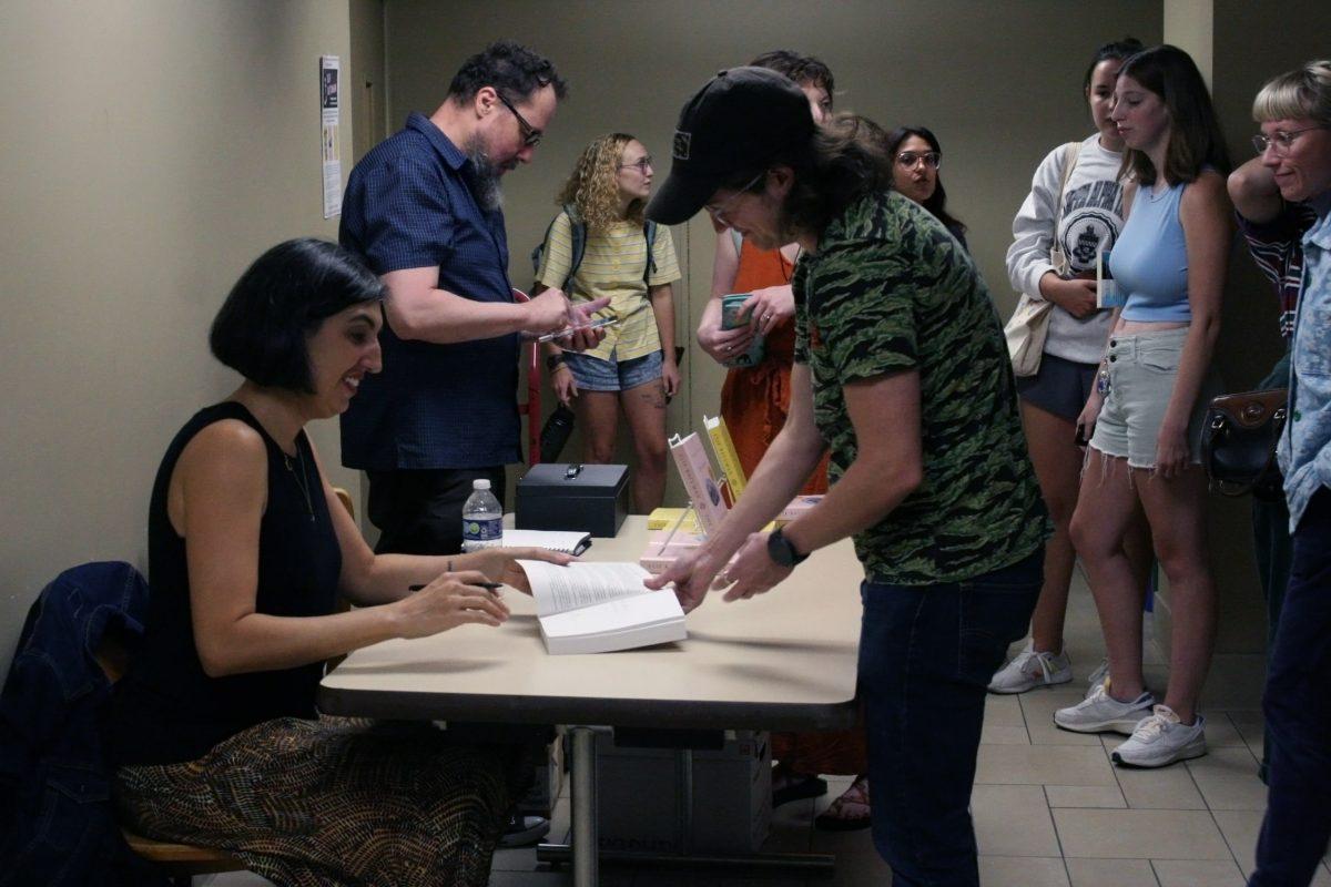 Elif Batuman sits at a table and signs a book for a fan who is standing in Tate Hall.