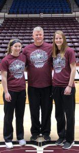 Hayley poses on a basketball court to the right of her coach and teammate. The three wear matching maroon shirts.