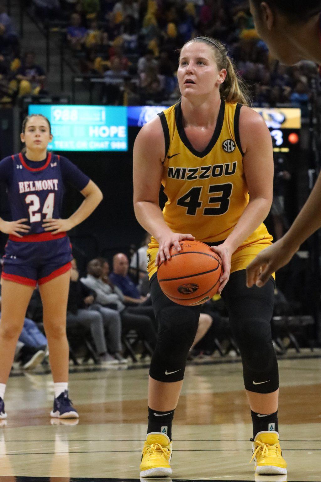Hayley, wearing a yellow jersey, crouches down with a basketball in her hands.