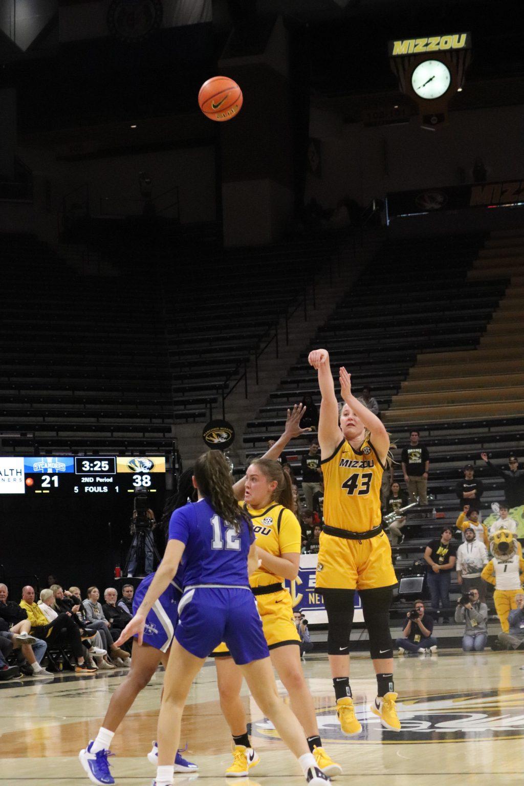 Hayley has her arms raised after throwing a basketball, which is in midair.