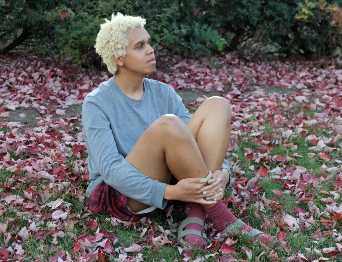 A MU student sits in the grass surrounded by the fallen red leaves outside Plaza 900.