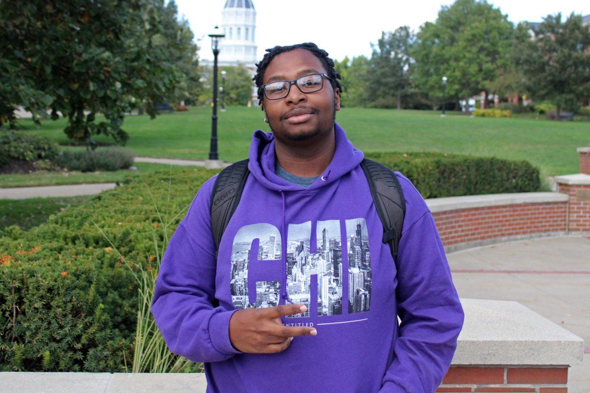 A man stands holding two fingers in a peace sign
