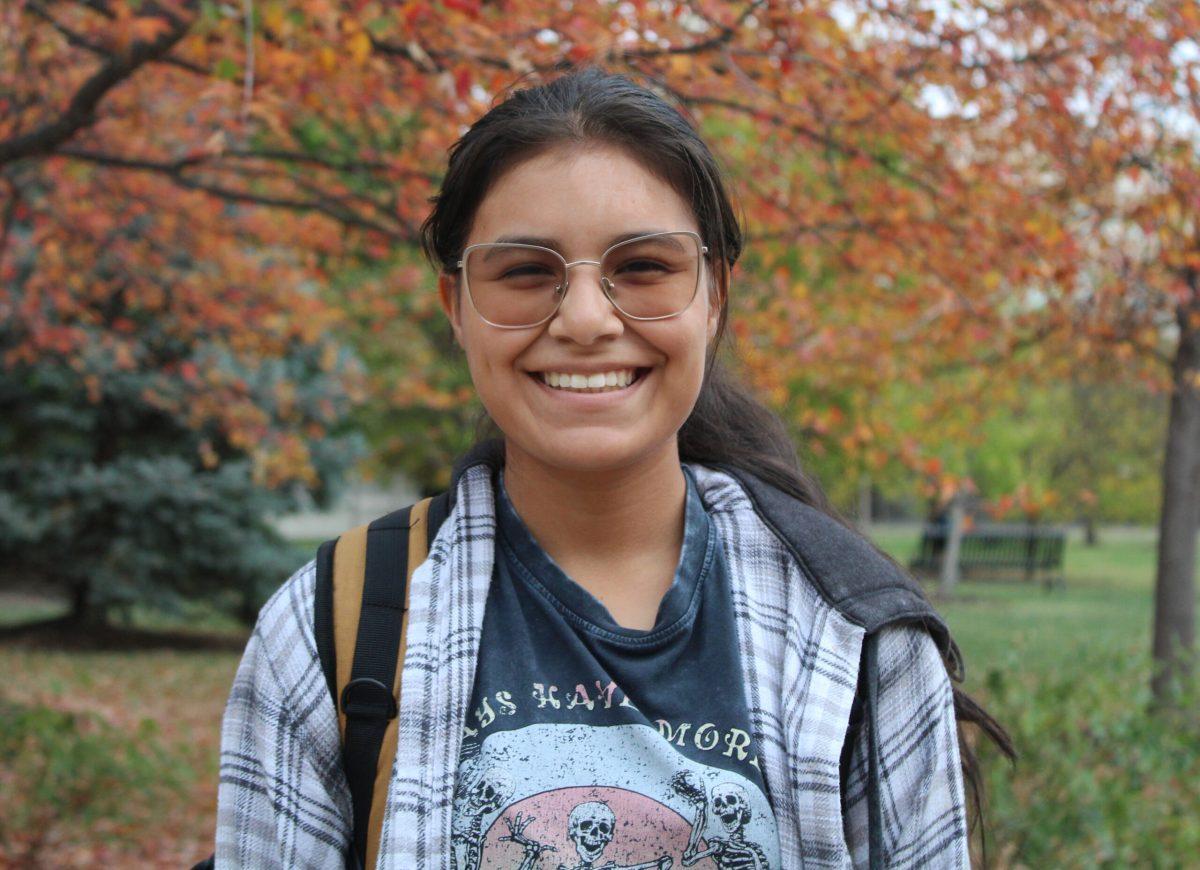 An MU student smiles outside of the MU Student Center with bright orange leaves on trees in the background.
