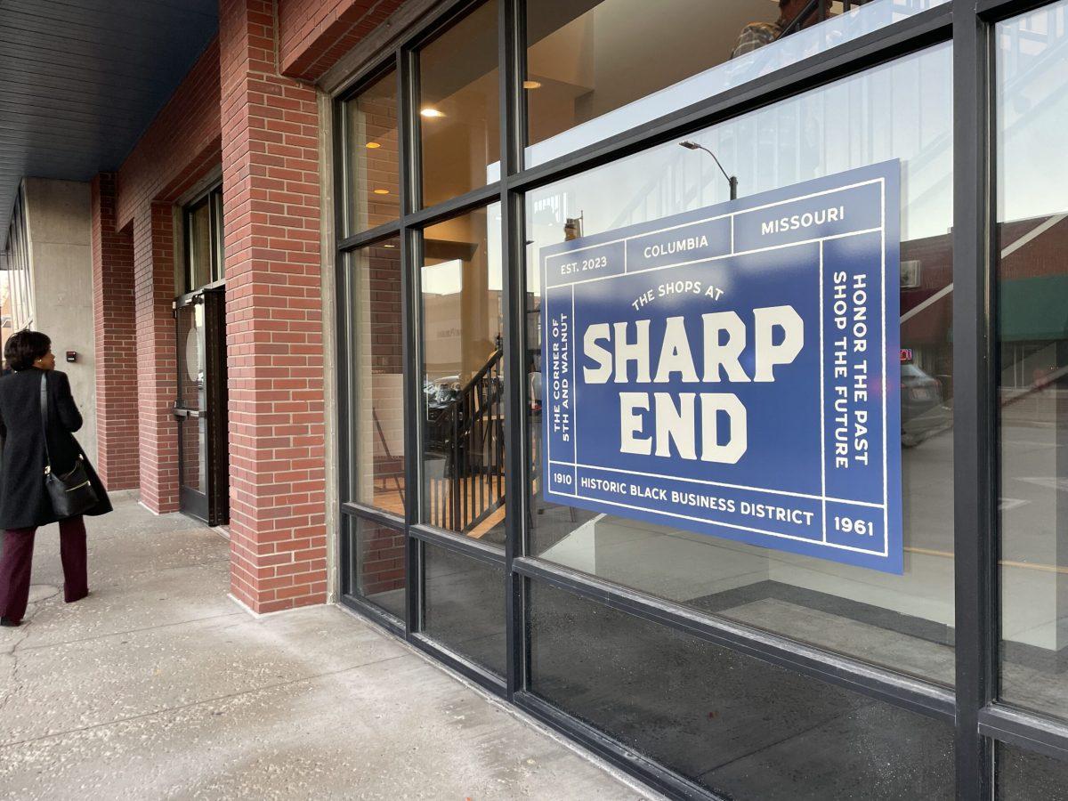 A woman enters The Shops at Sharp End, passing a sign with the business name.
