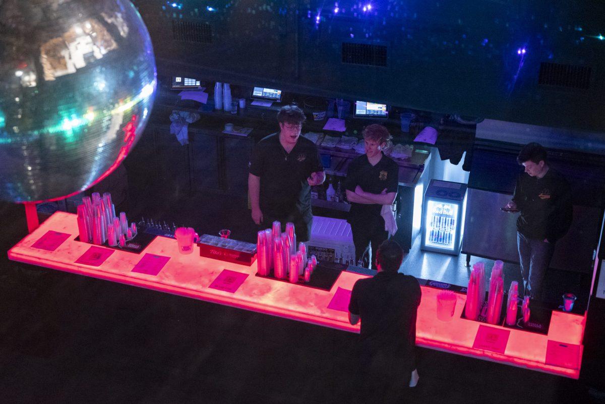 A group of bartenders sit around a bar below a disco ball.